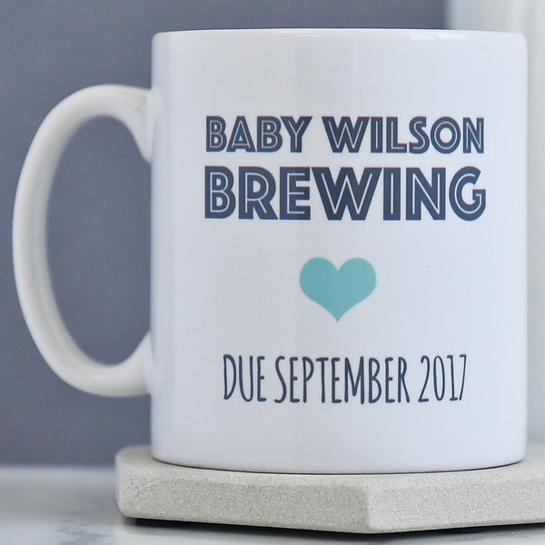 A white mug on a grey background. the mug has black font and a blue heart.
